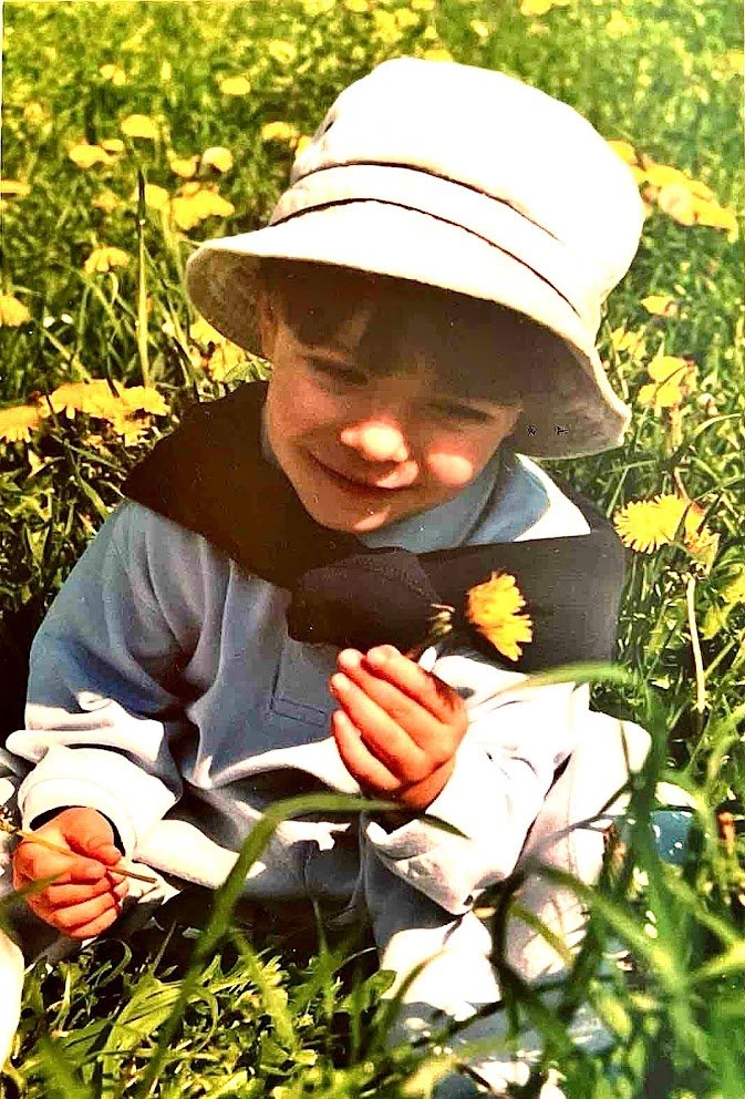 Pau de niño, observando una flor entre la hierba.